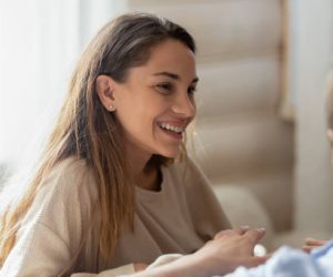 Head shot attractive happy young mixed race woman sitting on couch, listening to friend. Smiling wife communicating discussing chatting talking to husband, enjoying positive trustful conversation.