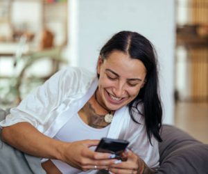 Young woman waking up in bed and checking her smartphone